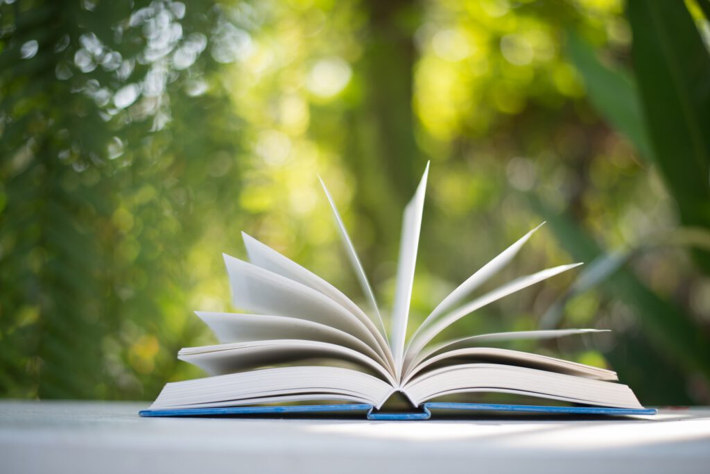 Close up of open book at home garden with nature bokeh background.